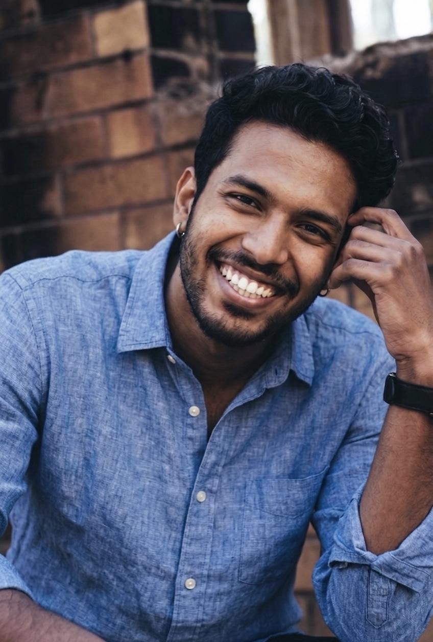 A young Indian man in a blue linen shirt laughing