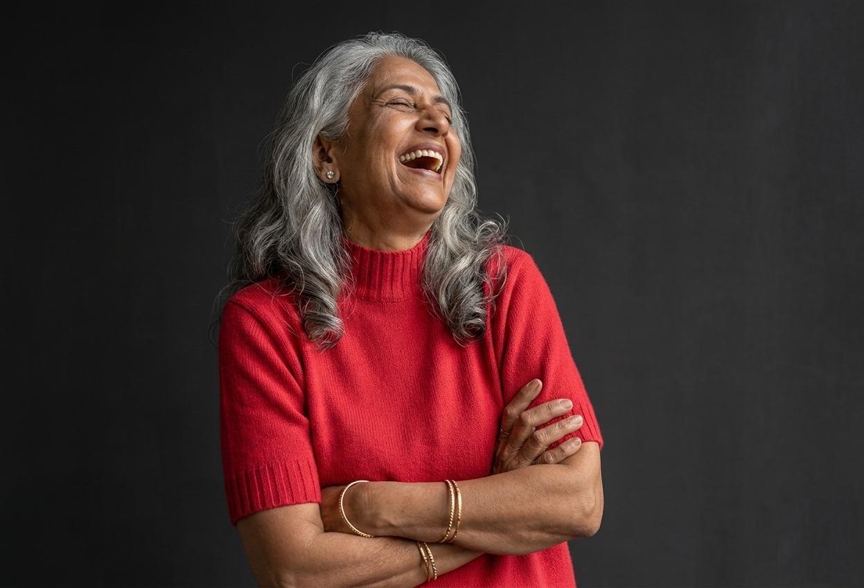 A silver-haired Indian woman in a red sweater laughing